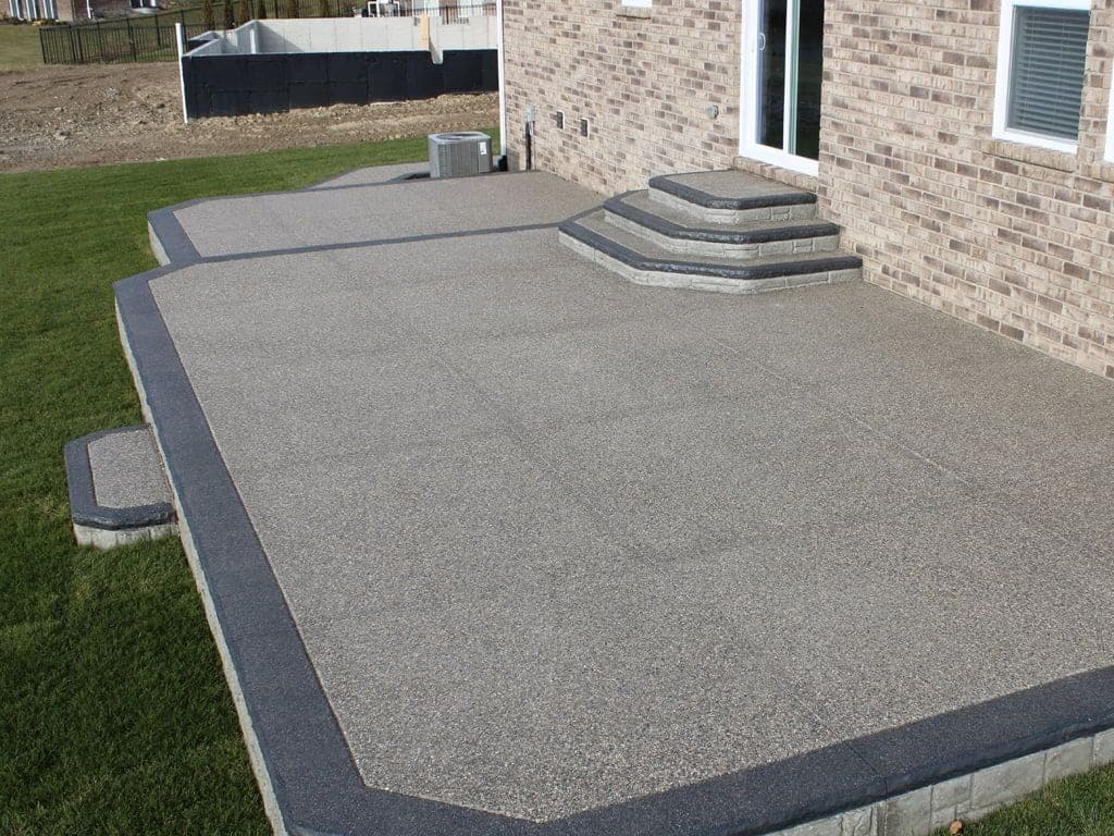 Exposed aggregate patio and steps sealed in a matte finish beside a brick home